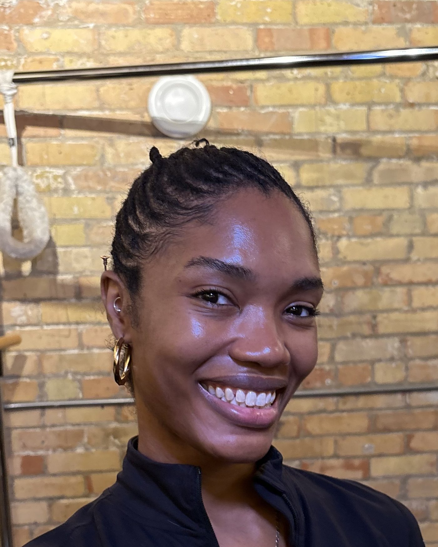 Ruqayyah in her downtown Toronto studio, smiling, the brick wall and the Cadillac frame behind her